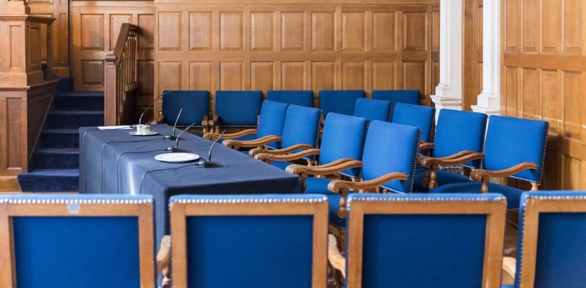 a wood-panelled court room with two rows of chairs in front of a table