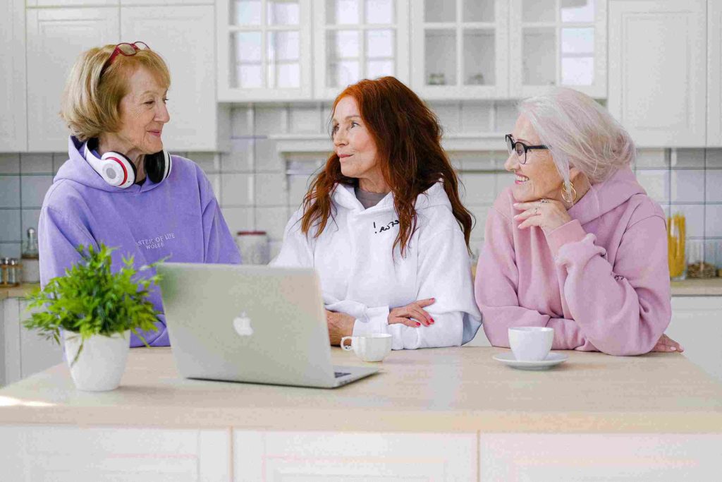 a group of elderly women around a laptop discussing new pension age policy